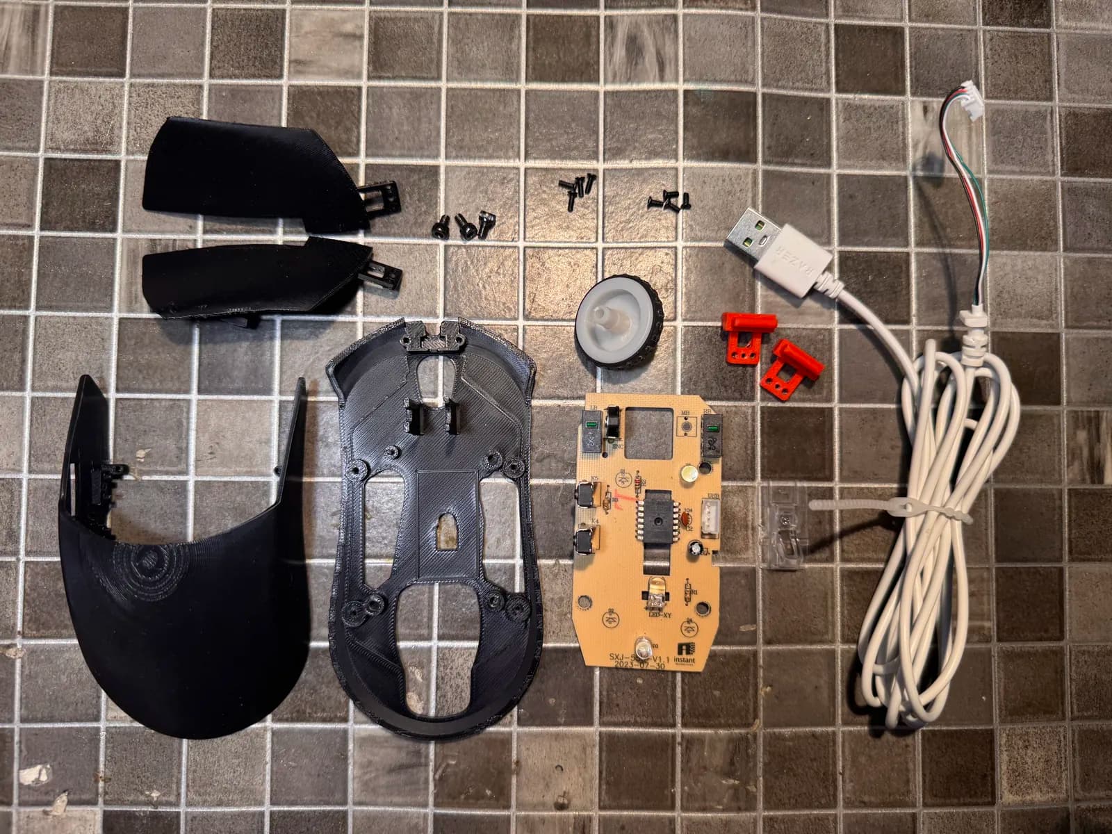 All the parts of the mouse laid out: printed top shell, base plate, buttons, PCB, scroll wheel, cable and screws